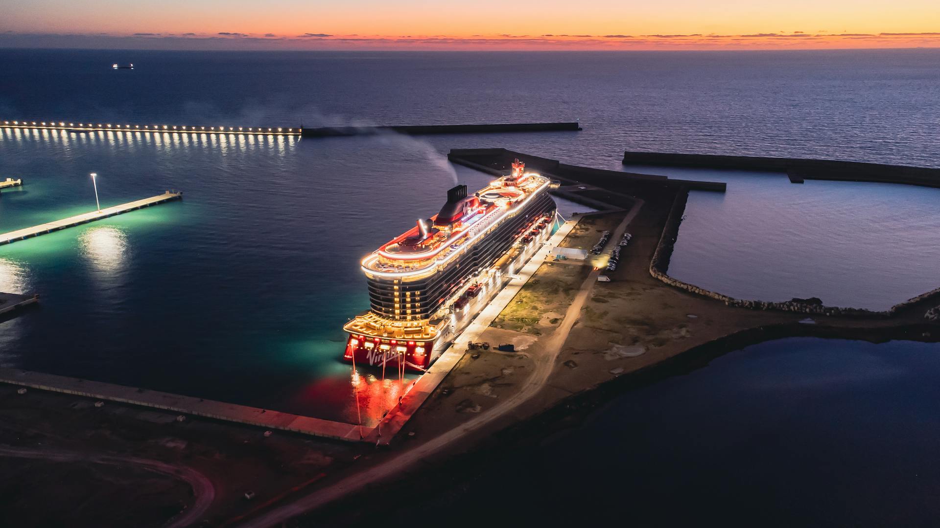 Aerial view of a brightly lit cruise ship docked at a port during sunset in Civitavecchia, Italy.