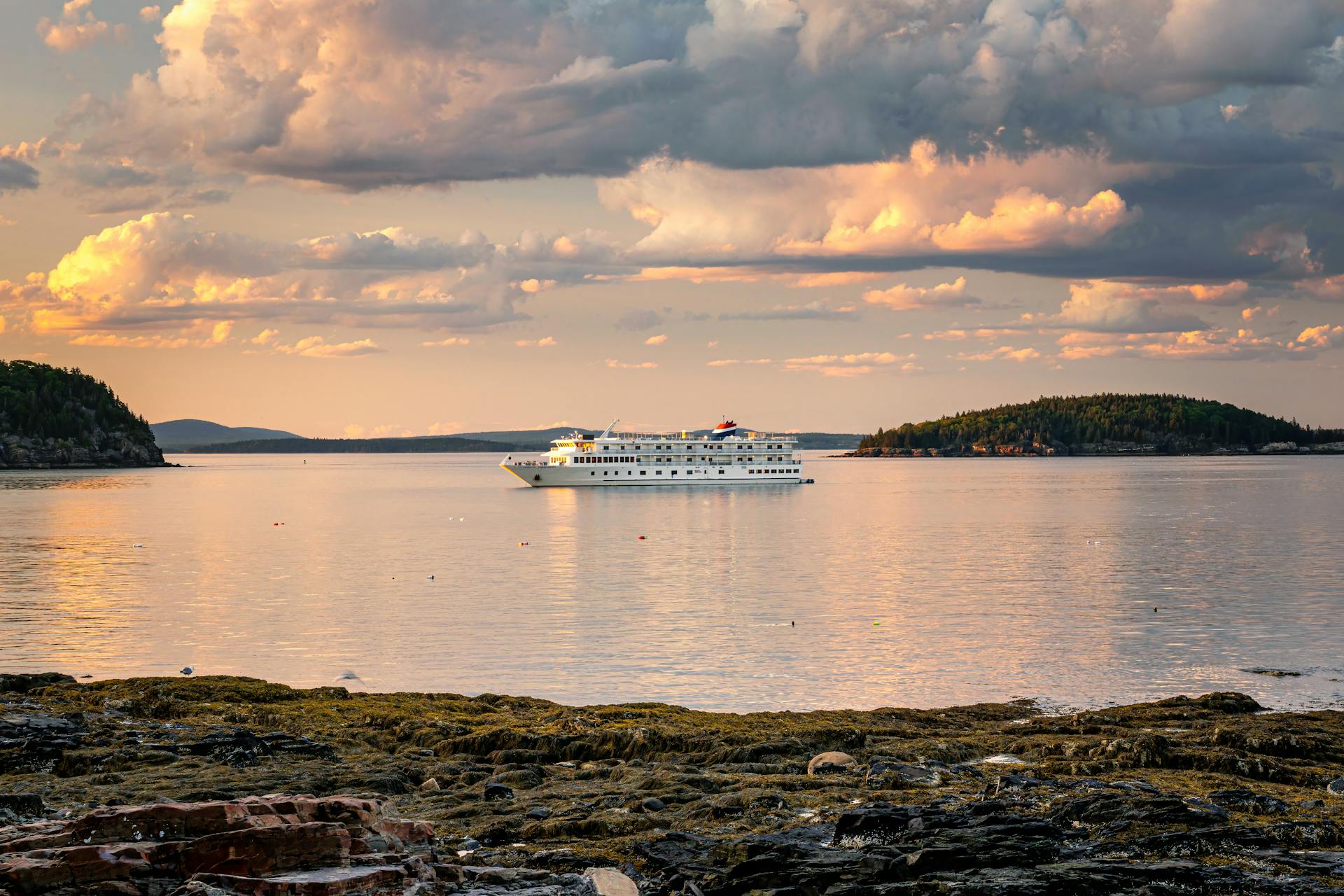A luxurious cruise ship sailing tranquil waters under a dramatic cloudy sky at sunset.