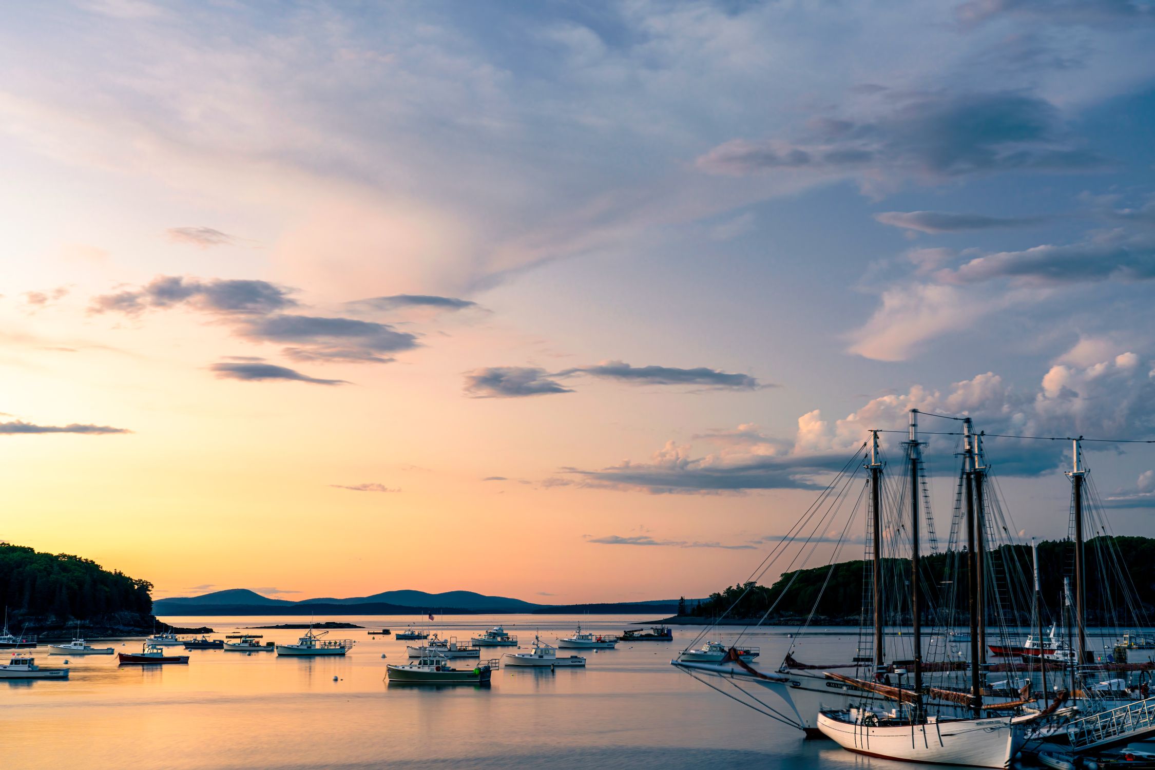 Serene sunset view over a calm harbor filled with sailboats and yachts.