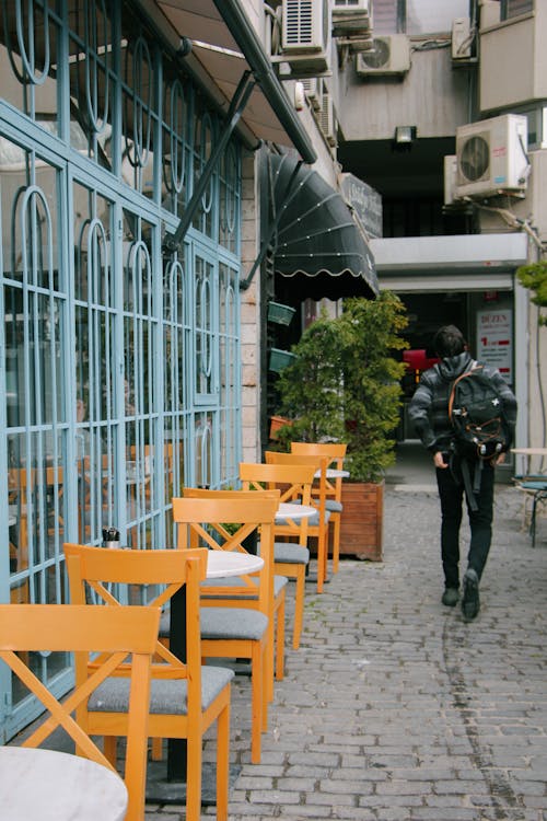 Man Walking near Chairs and Tables on Alley in Town