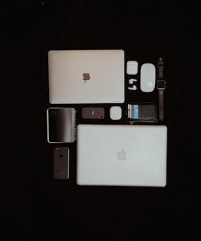 Top view of modern apple electronics including laptops, smartphone, and accessories on a dark background.