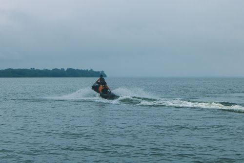 Free A man rides a jet ski, creating waves on a cloudy day at sea, showcasing an adventurous moment. Stock Photo