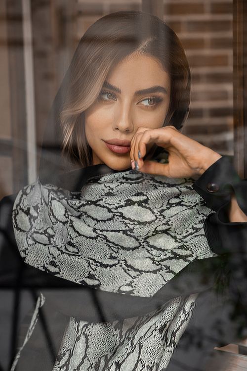 Free Stylish woman with snake print scarf peering thoughtfully through glass window. Stock Photo