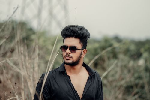 Free Confident man with sunglasses posing in a natural setting, wearing a sleek black shirt. Stock Photo