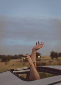Hands reaching out of a car sunroof on a road trip, symbolizing freedom and adventure.