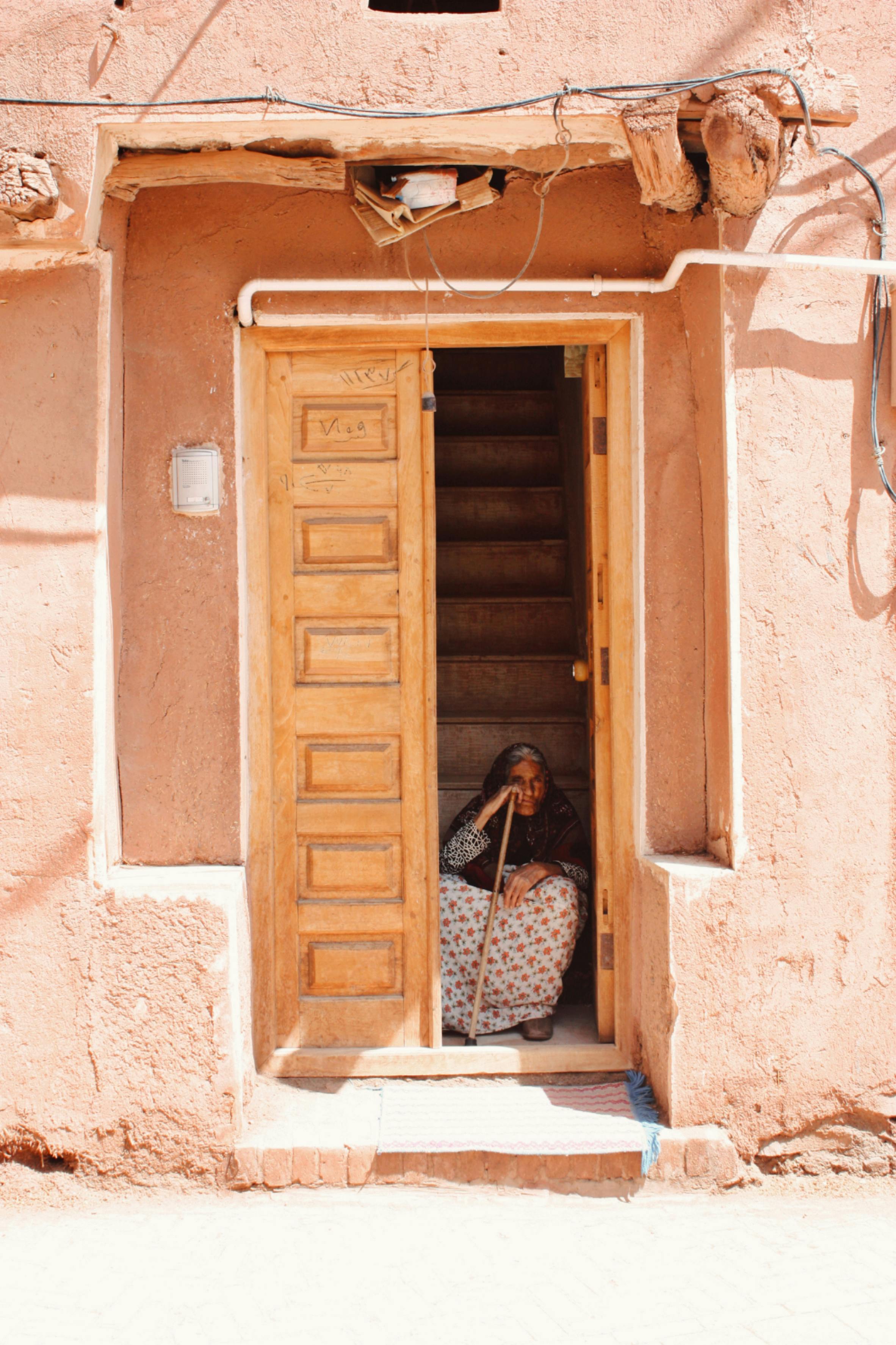 Elderly woman in a traditional doorway in Abyaneh, Iran, showcasing local architecture.