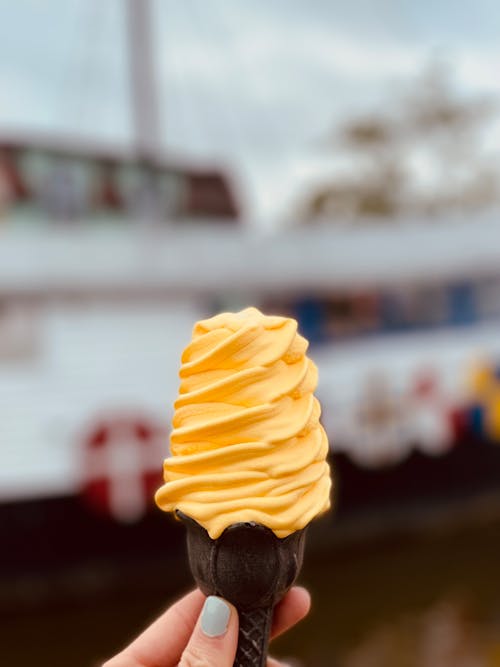 A Person Holding a Brown Cone with Yellow Ice Cream on Top
