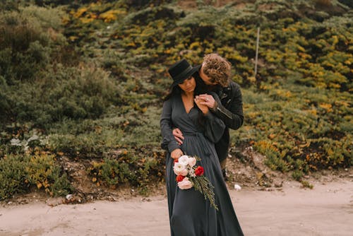 A Man Hugging a Pregnant Woman while Standing Near Green Plants