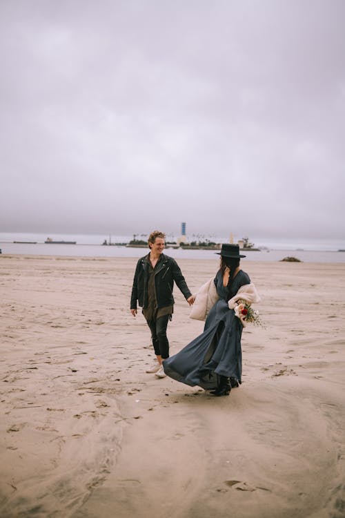 A Couple Holding Hands and Walking on a Beach