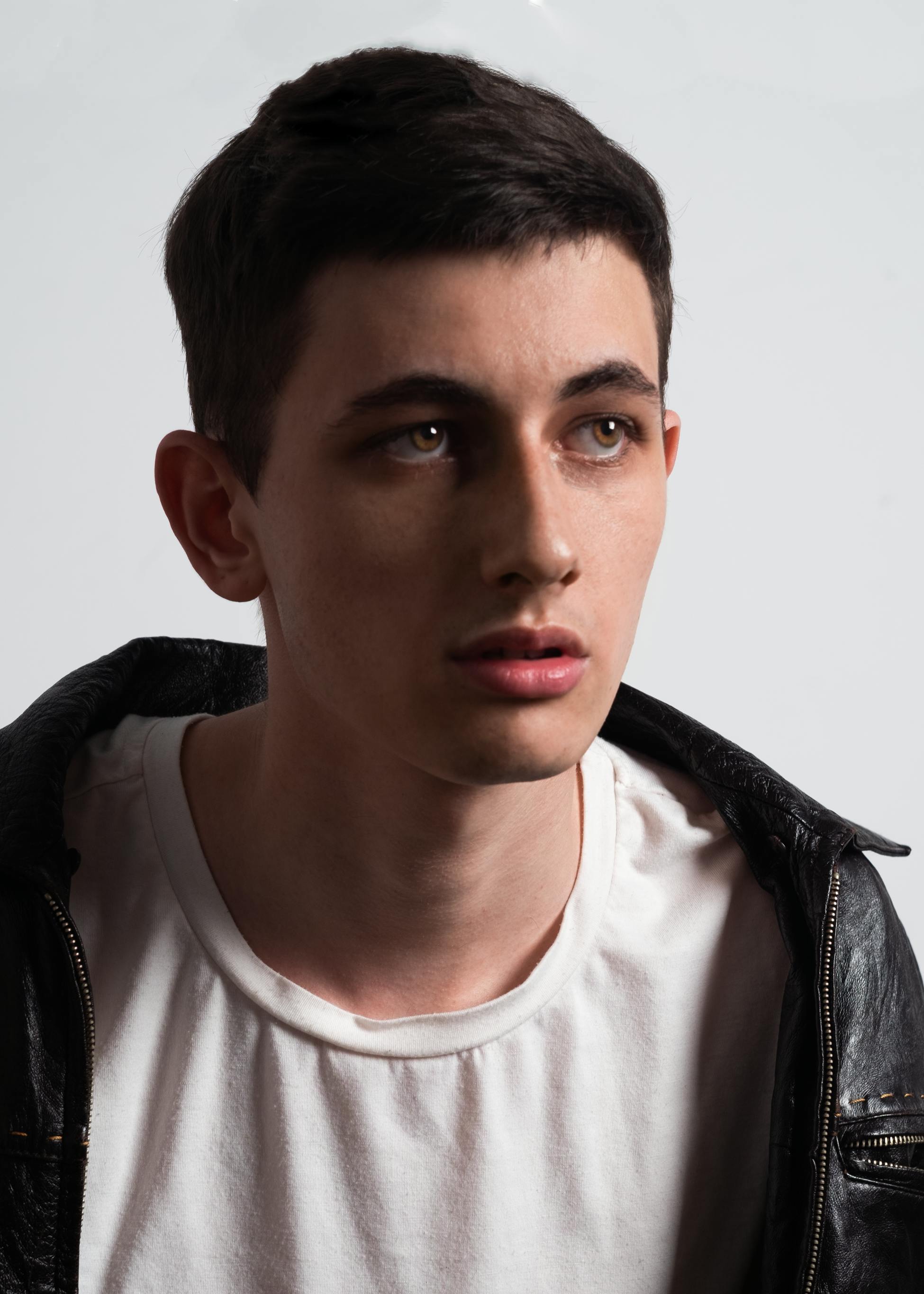 A young man in a black leather jacket and white shirt, looking pensive.