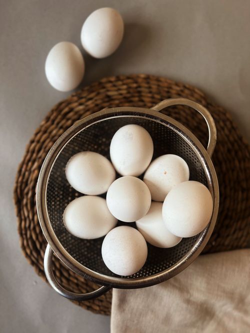 Free Close-up of white eggs in a metallic colander on a woven mat, perfect for food photography. Stock Photo