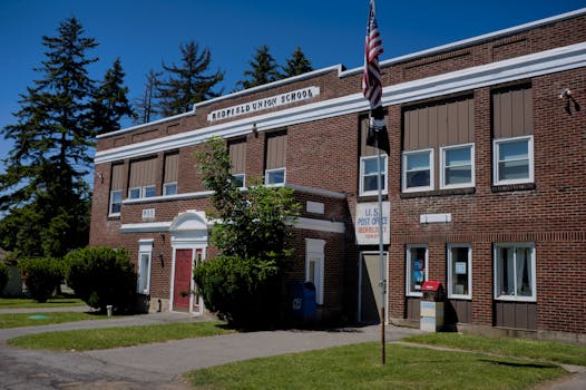 A classic brick schoolhouse in Redfield, NY with a U.S. Post Office, capturing a sunny day.