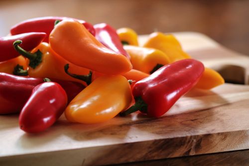 Free Vibrant red, yellow, and orange bell peppers displayed on a rustic wooden chopping board. Stock Photo