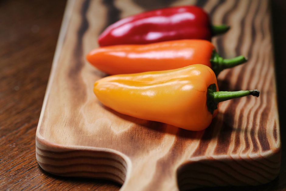 Halved red, yellow, and orange sweet peppers with blistered, charred skins on a baking sheet fresh from the oven.