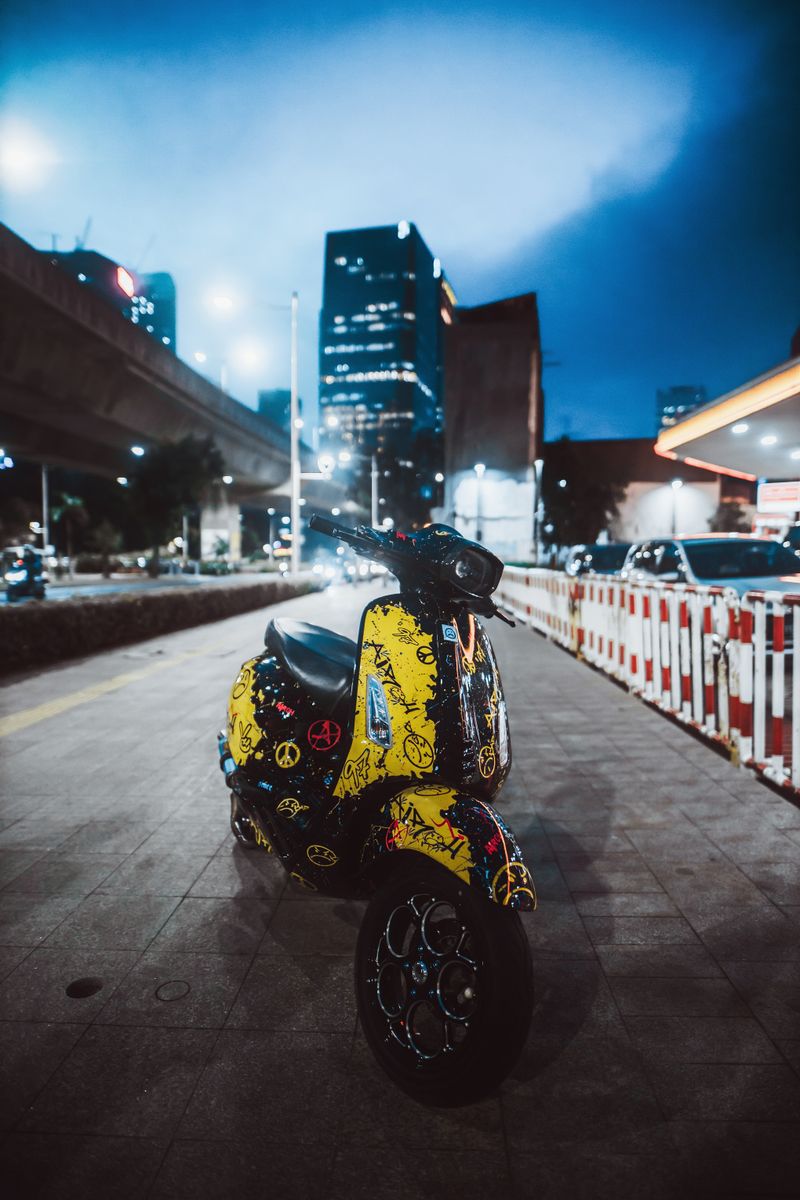 A vibrant scooter parked on a city street at night with skyscrapers