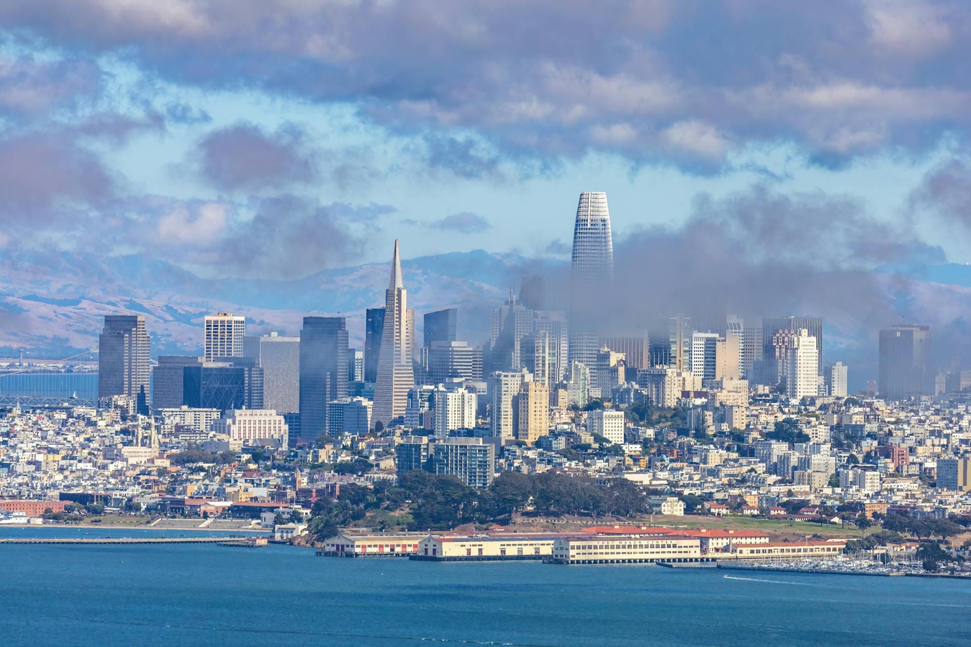 San Francisco skyline featuring the Salesforce Tower under a cloudy sky, captured from an aerial view.