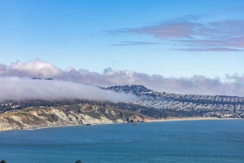 Free Stunning aerial view of a coastal city skyline with rolling clouds and blue ocean waters. Stock Photo