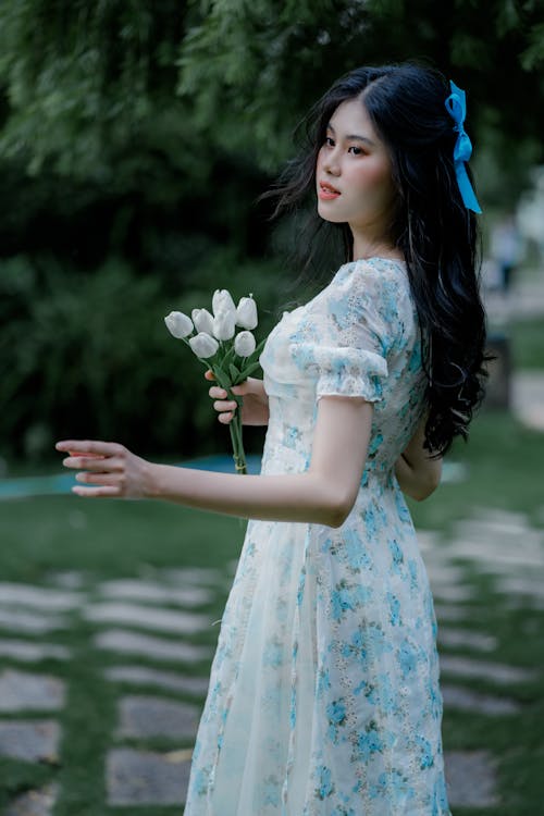 A Woman in White and Blue Floral Dress Holding White Flowers