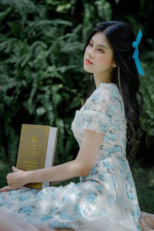 A Woman in White Floral Dress Holding a Brown Book