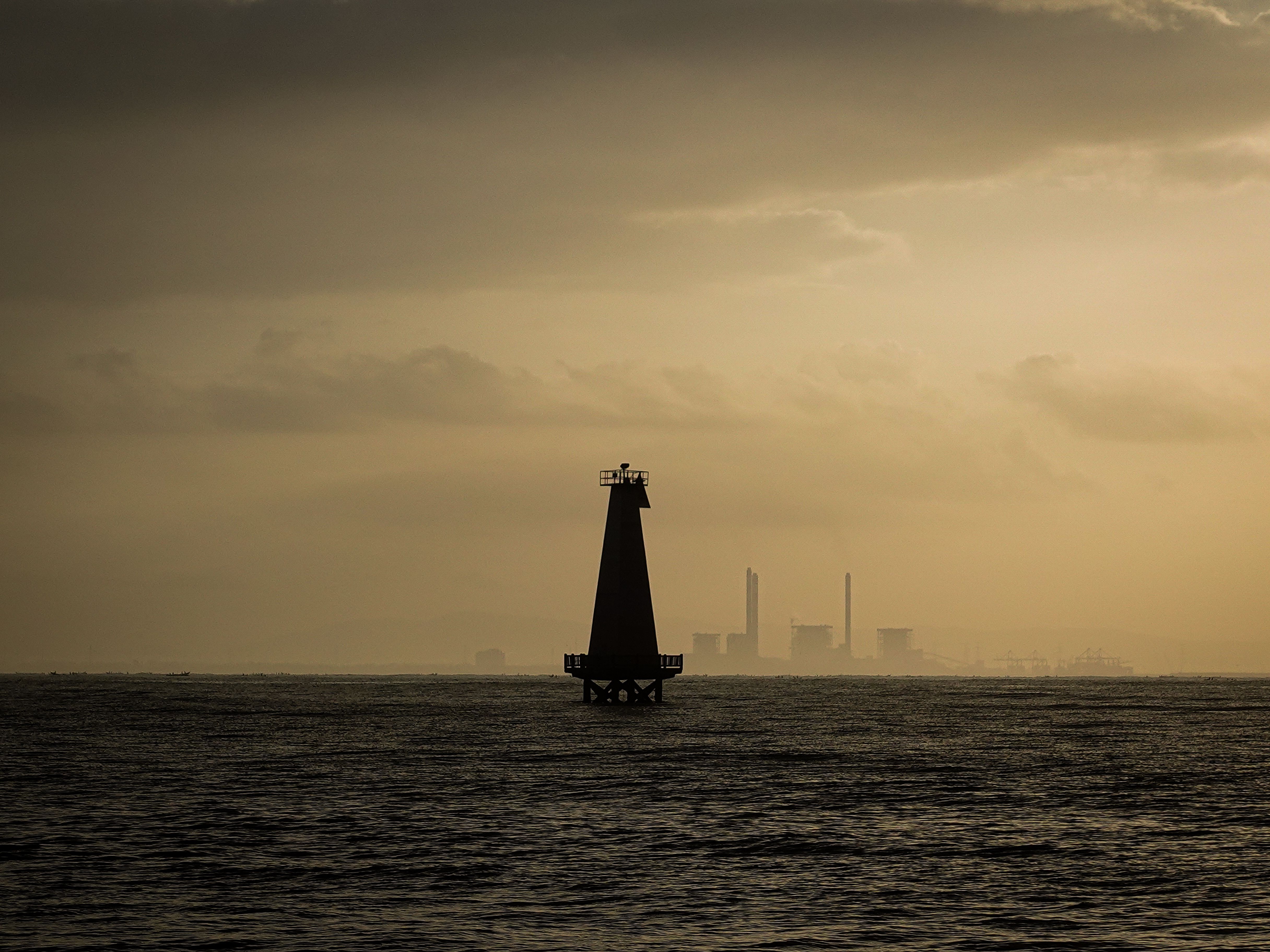Ethereal view of a lighthouse at sunset with industrial backdrop in Central Java.