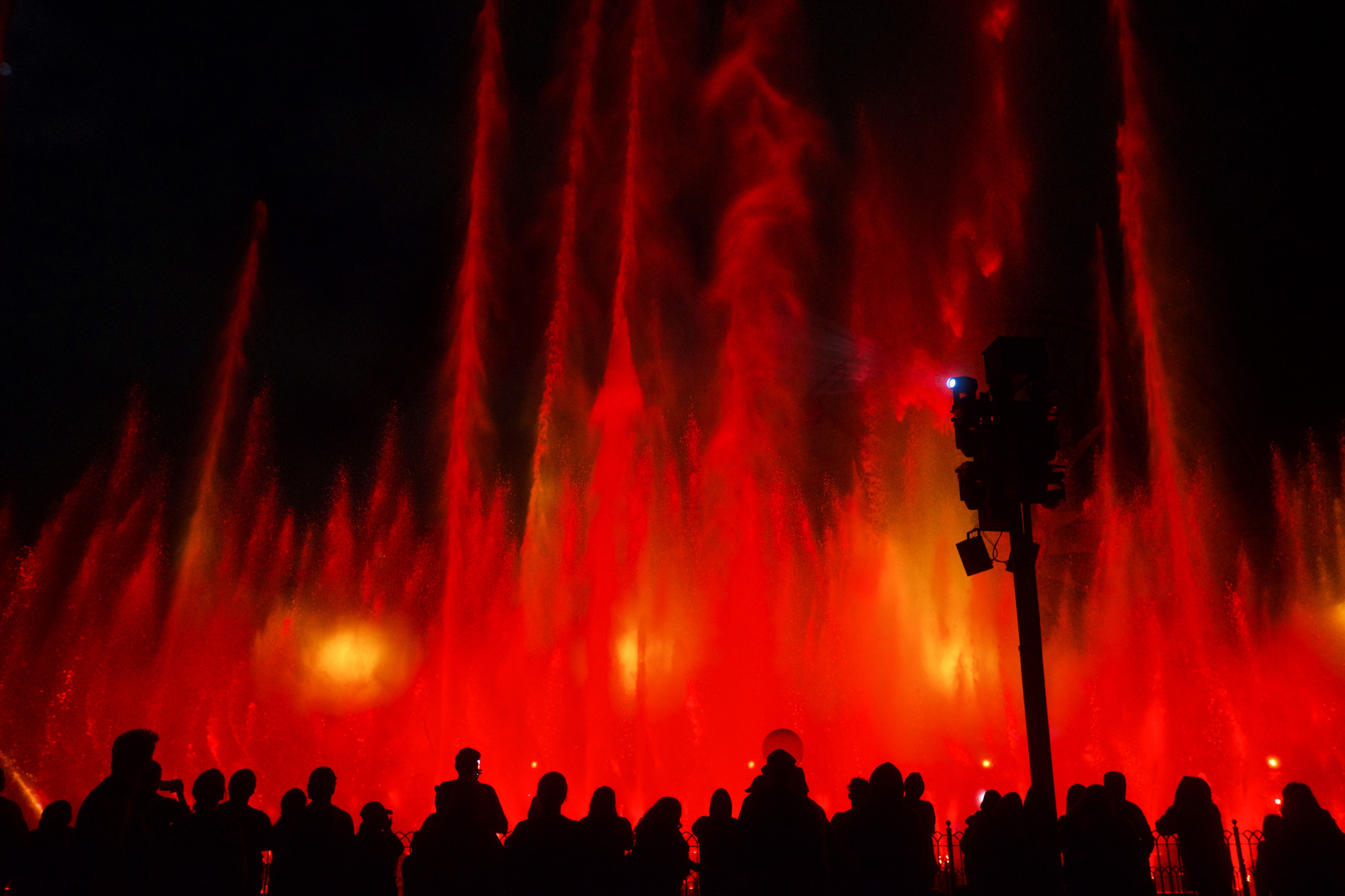 Silhouettes watching a vibrant water fountain show with red lighting in Anaheim at night.