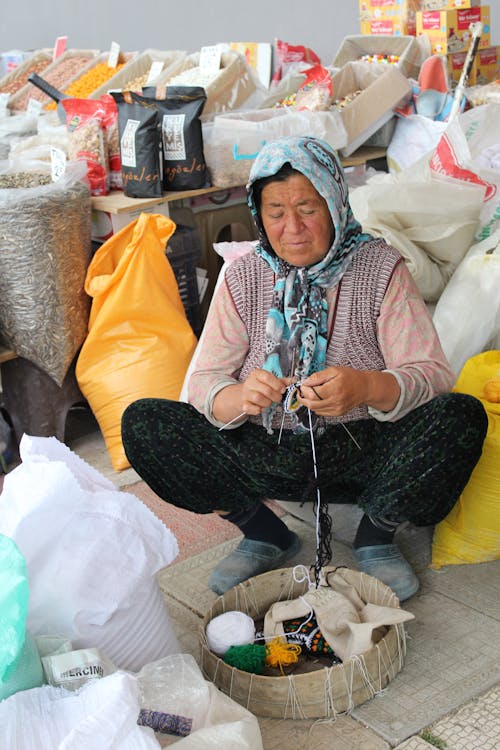 Senior Woman Wearing a Headscarf Knitting, and Bags of Seeds in Background