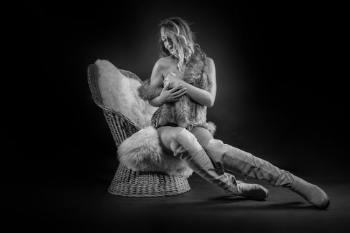 Free Black and white studio portrait of woman in fur and boots on a woven chair. Stock Photo