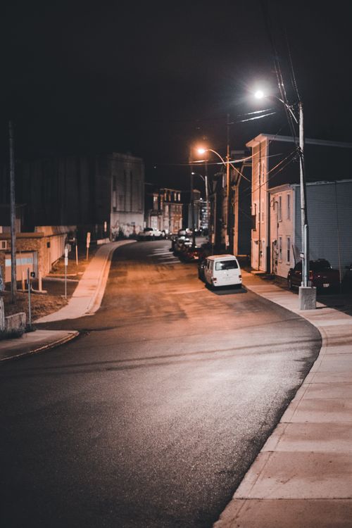 Free A quiet urban street scene at night featuring parked vehicles and warm streetlights. Stock Photo