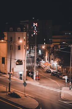 Aerial view of an urban street at night with illuminated buildings and parked cars.