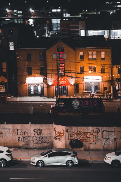 Free Aerial view of an illuminated urban street with graffiti and parked cars at night. Stock Photo