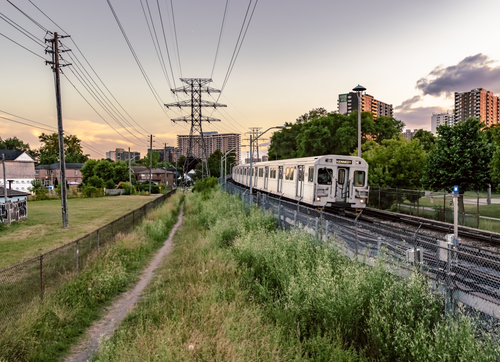Free Toronto subway train passing through greenery during sunset with urban skyline. Stock Photo