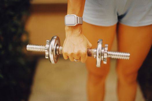 Close-up of a woman lifting a dumbbell, wearing a smartwatch, focusing on fitness and exercise.