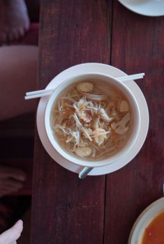 Top view of a flavorful Asian noodle soup with fresh vegetables served with chopsticks on a wooden table.