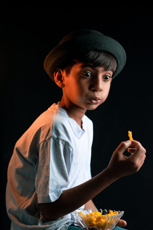 Photograph of a Boy with a Hat Eating a Chip