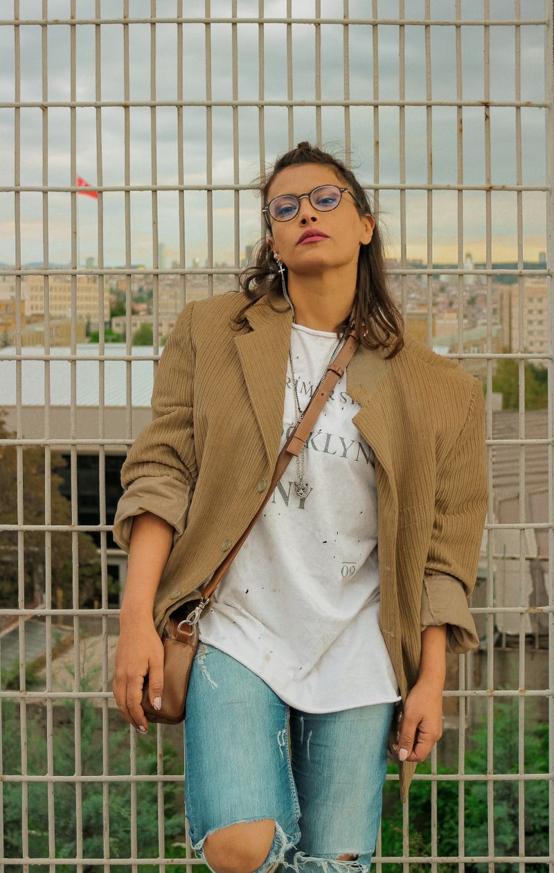 Woman in beige blazer and jeans leaning on metal fence, soft professional outfit