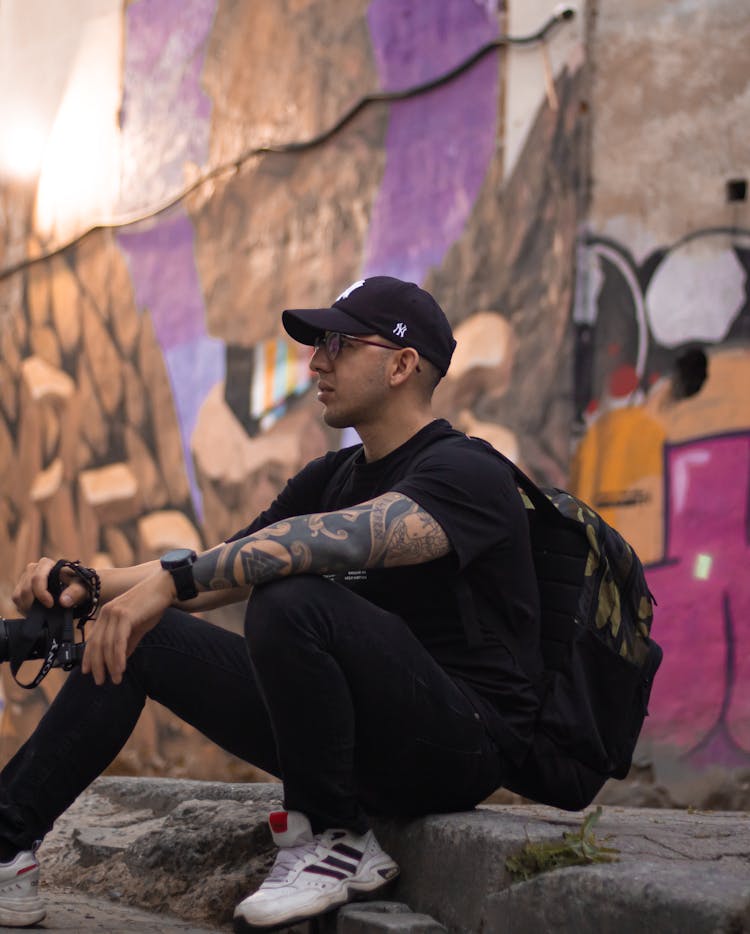 A Photographer In A Black Outfit Sitting On A Curb