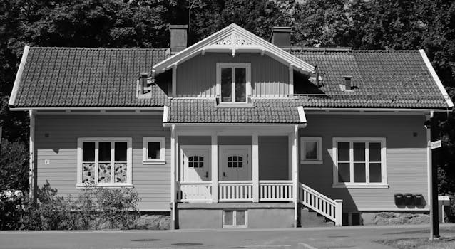 Black and white image of a charming wooden house facade with porch in suburban area.