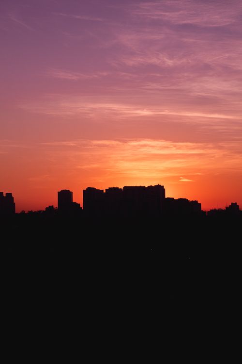 Free A stunning city skyline silhouette with a vibrant orange and purple sunset backdrop. Stock Photo