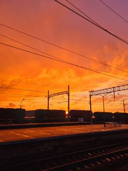 Vibrant sunset over Saint Petersburg railway station platform, with dramatic orange and pink sky.