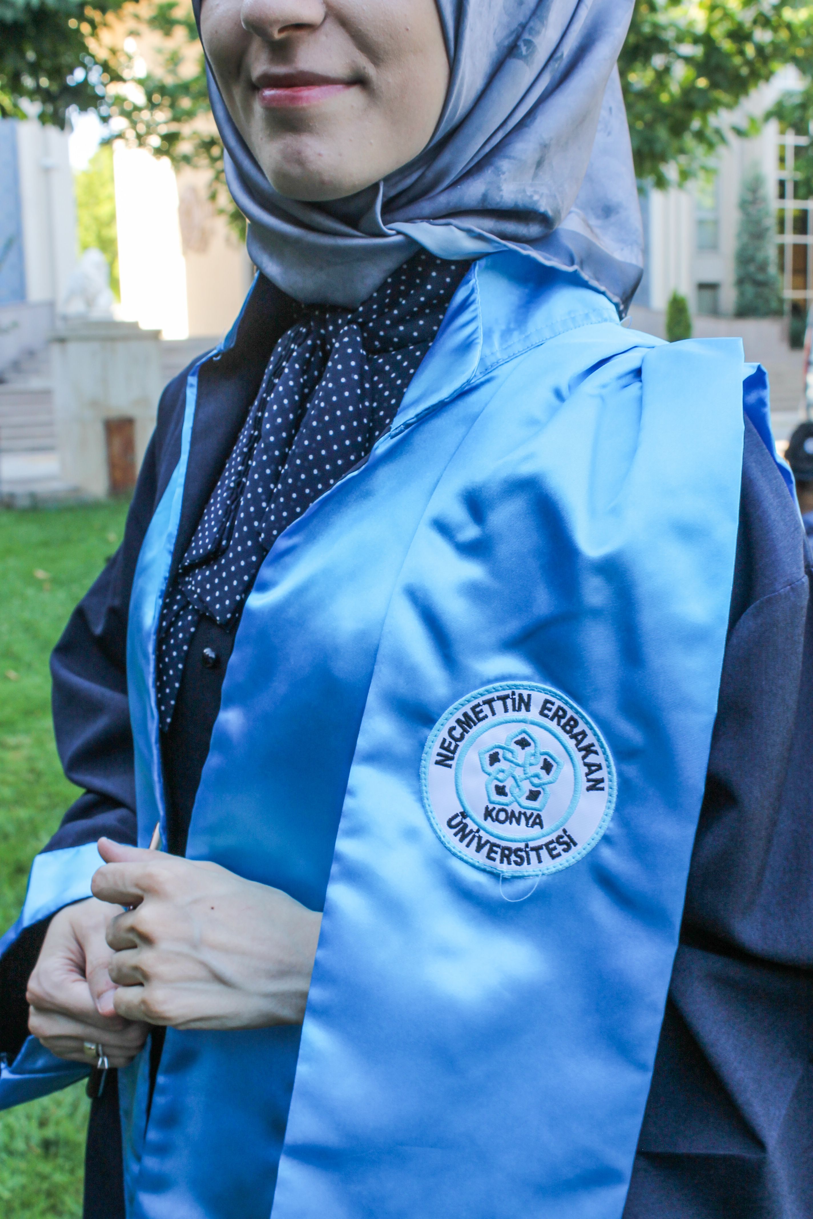 A graduate wearing academic regalia at Necmettin Erbakan University campus outdoors.