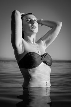 Striking swimwear portrait of a woman in water, arms raised, in black and white.