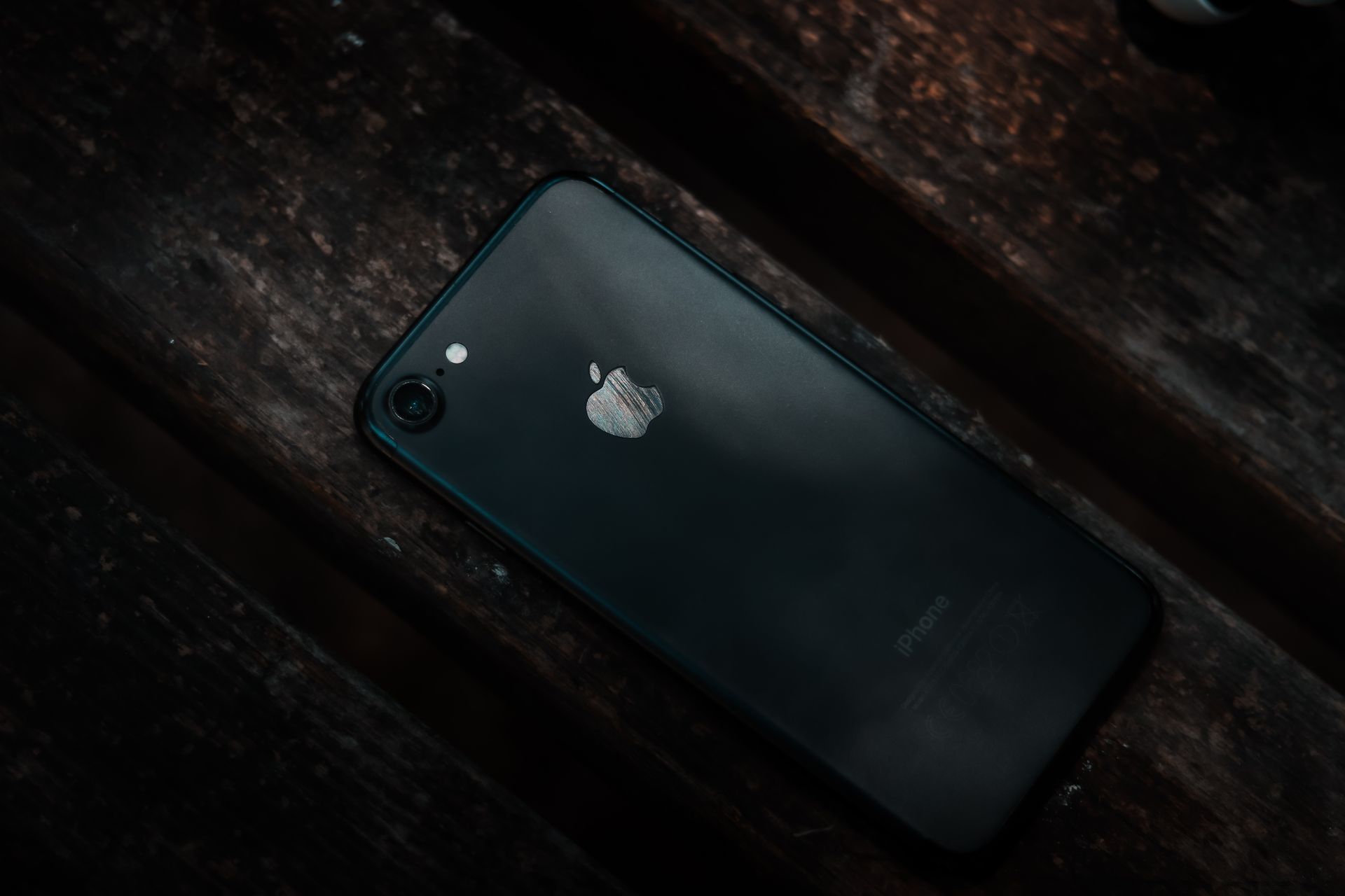 A black smartphone with logo visible, resting on a rustic wooden surface.