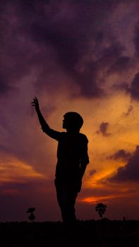 Silhouette of a person with raised hand against a dramatic orange and purple sunset sky in Sasaram, India.. pexels, silhouett
