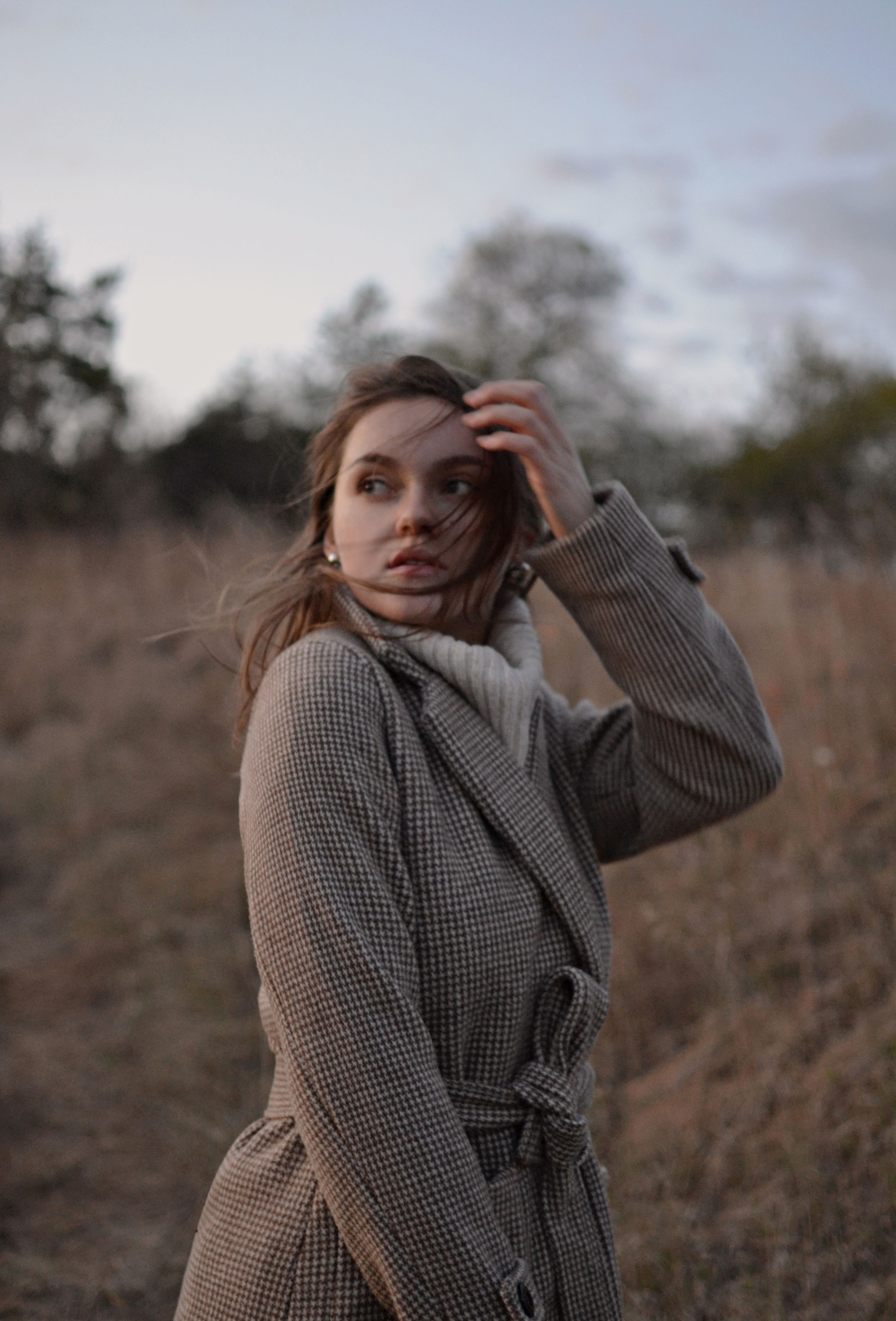 Portrait of a woman in a coat amidst a windy, natural outdoor setting.