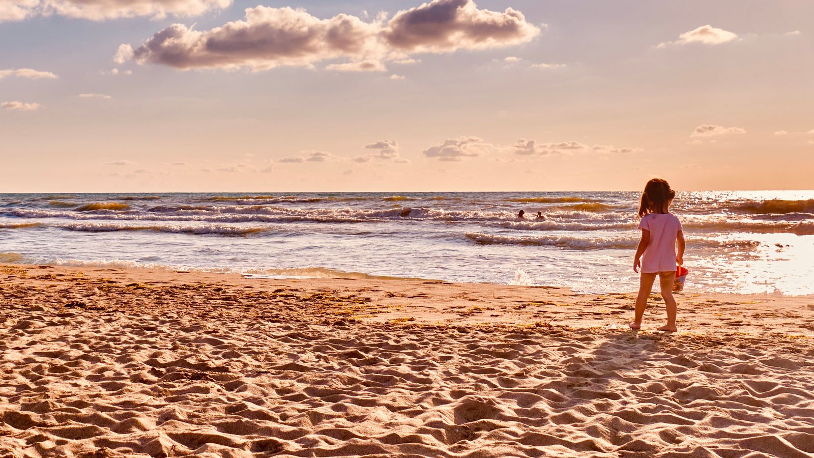 A young girl standing on the sand at the water's edge on a sunny evening in Durrës