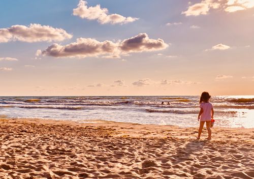 Free A young girl plays on the sandy beach at Durrës, Albania, during a sunny day with calm waves. Stock Photo