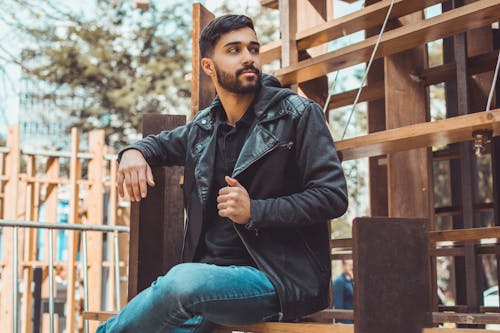 Free Man Wearing Black Jacket and Jeans Sitting on Brown Wooden Chair Stock Photo