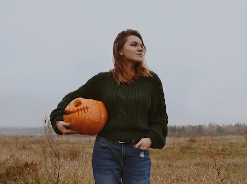 Young Woman Standing Outdoors With a Jack O Lantern in Hand