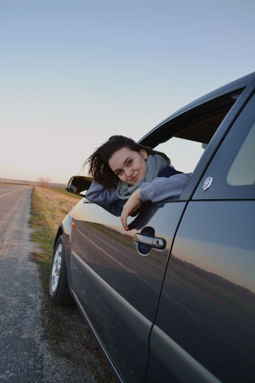Free A woman gazes out from a car window on an open road, capturing the essence of travel and freedom. Stock Photo