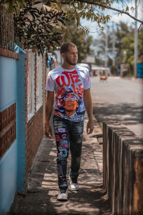 Free Man walking on a sunny sidewalk wearing a graphic T-shirt and jeans. Stock Photo